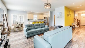 Un salon moderne avec un canapé bleu clair, un coin repas avec des chaises jaunes et une cuisine avec des meubles blancs.
