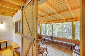Eine Holzblockhütte mit Veranda, Bänken, Schaukelstühlen und einem Ventilator.