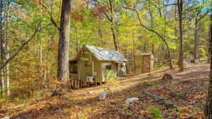A rustic cabin with a metal roof, surrounded by a forest with autumn-colored leaves. - Secluded Tallassee Cabin w/ Fire Pit & Porch! (Tallassee)