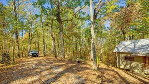 A forested area with a cabin and a vehicle on a dirt path. - Secluded Tallassee Cabin w/ Fire Pit & Porch! (Tallassee)