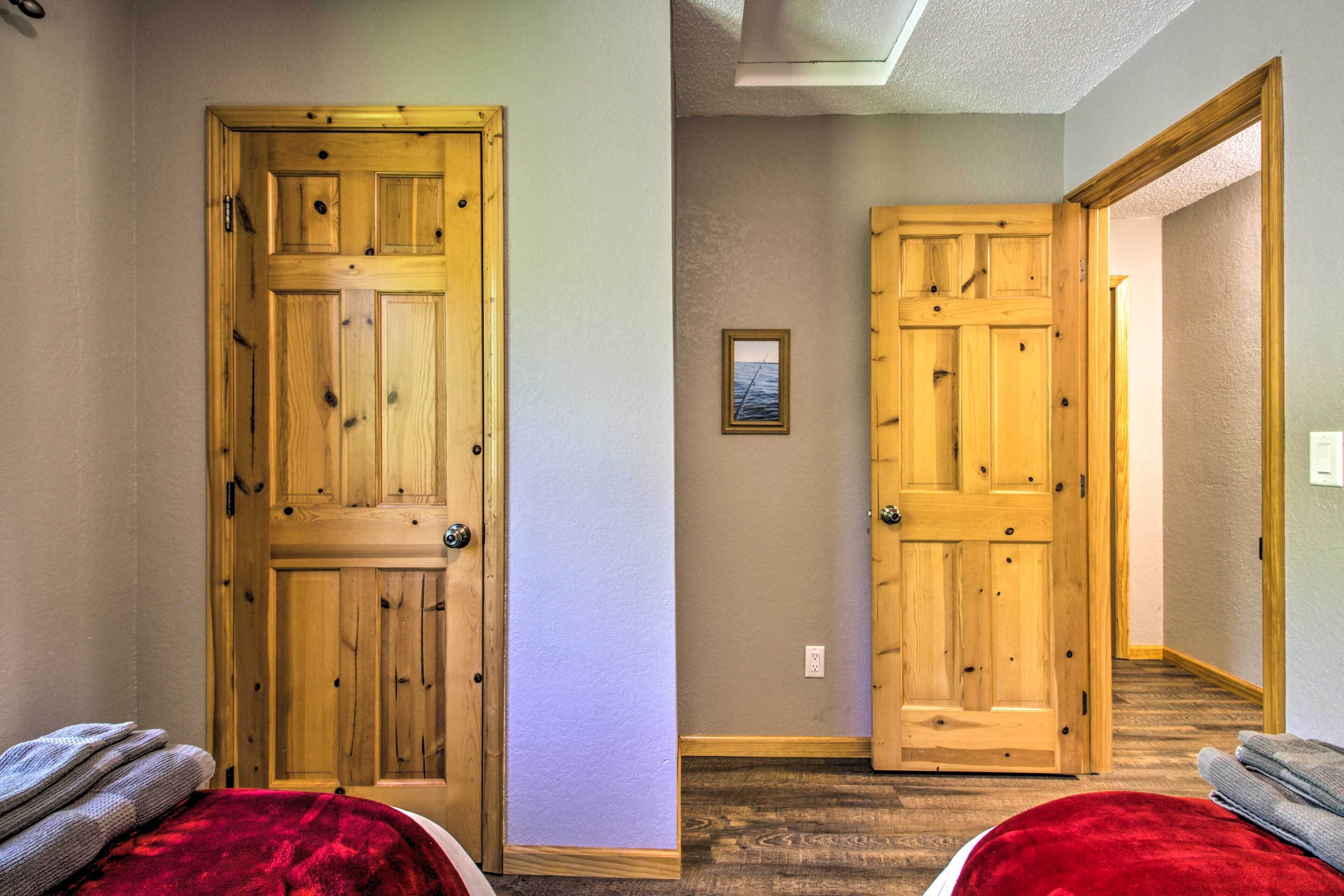 A room with a wooden door, a framed picture on the wall, and a red blanket on the bed.