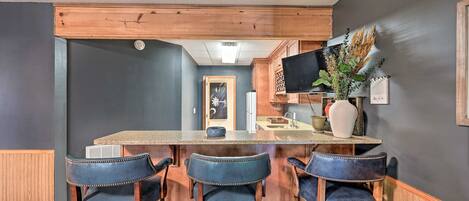 A kitchen with a bar area, dark walls, wooden ceiling beams, and bar stools.