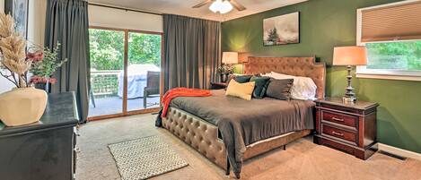 A bedroom with a large bed, a ceiling fan, a nightstand with a lamp, and a view of the outdoors through a sliding door.