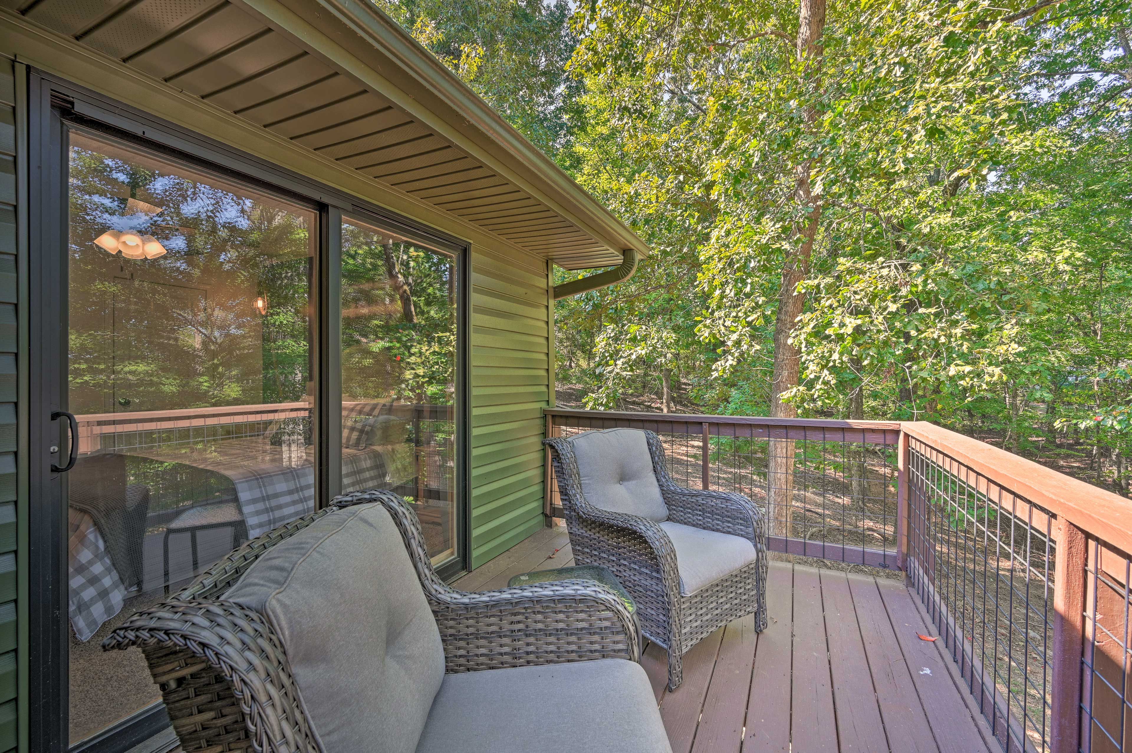 A covered deck with wicker furniture and a glass door leading to a wooded area.