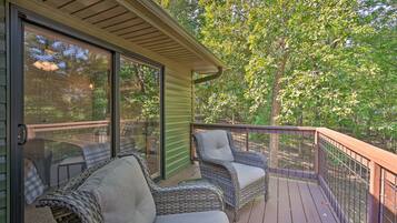 A covered deck with wicker furniture and a glass door leading to a wooded area.