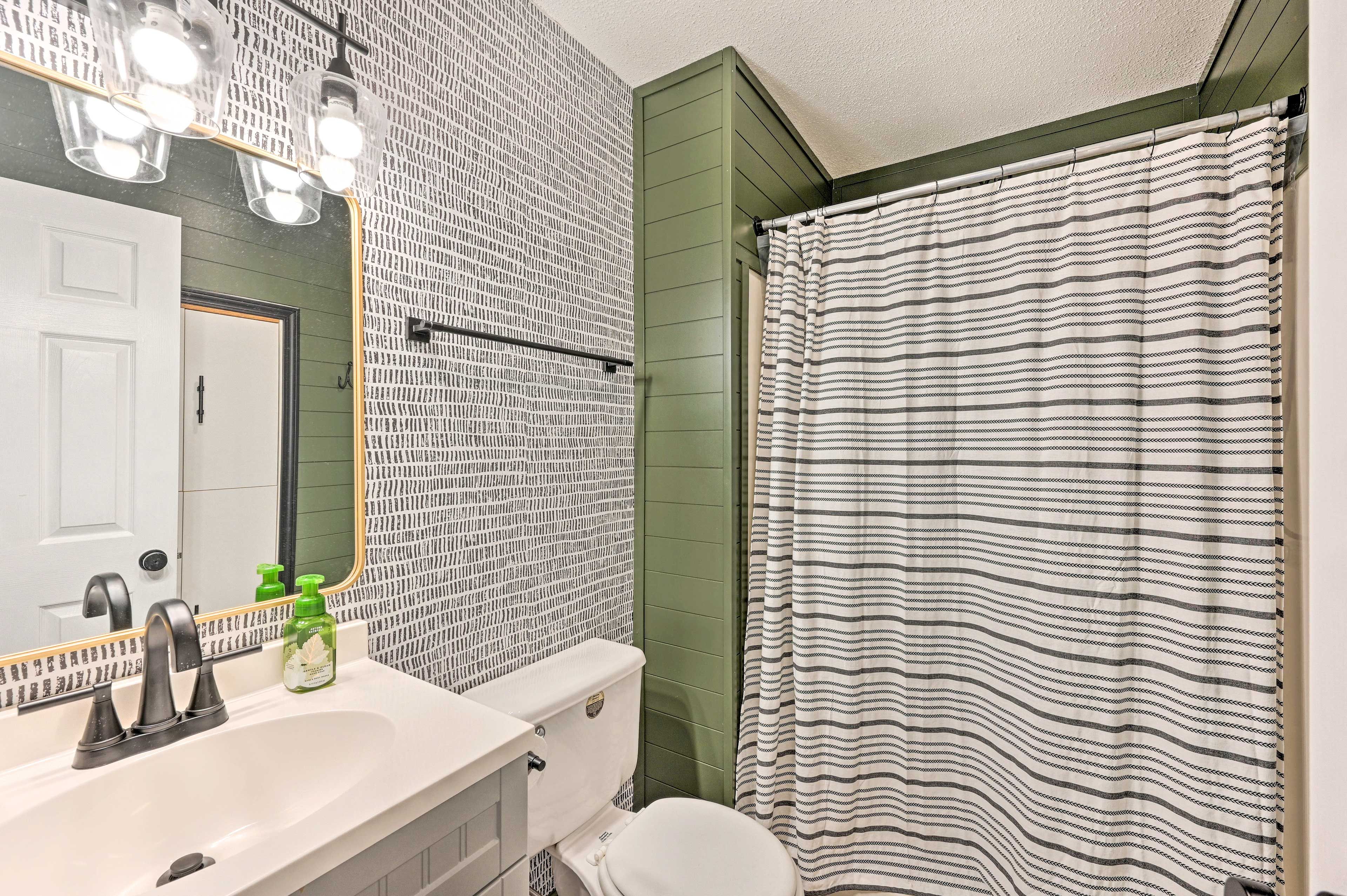 A bathroom with a white sink, green walls, a striped shower curtain, and a mirror with lights.