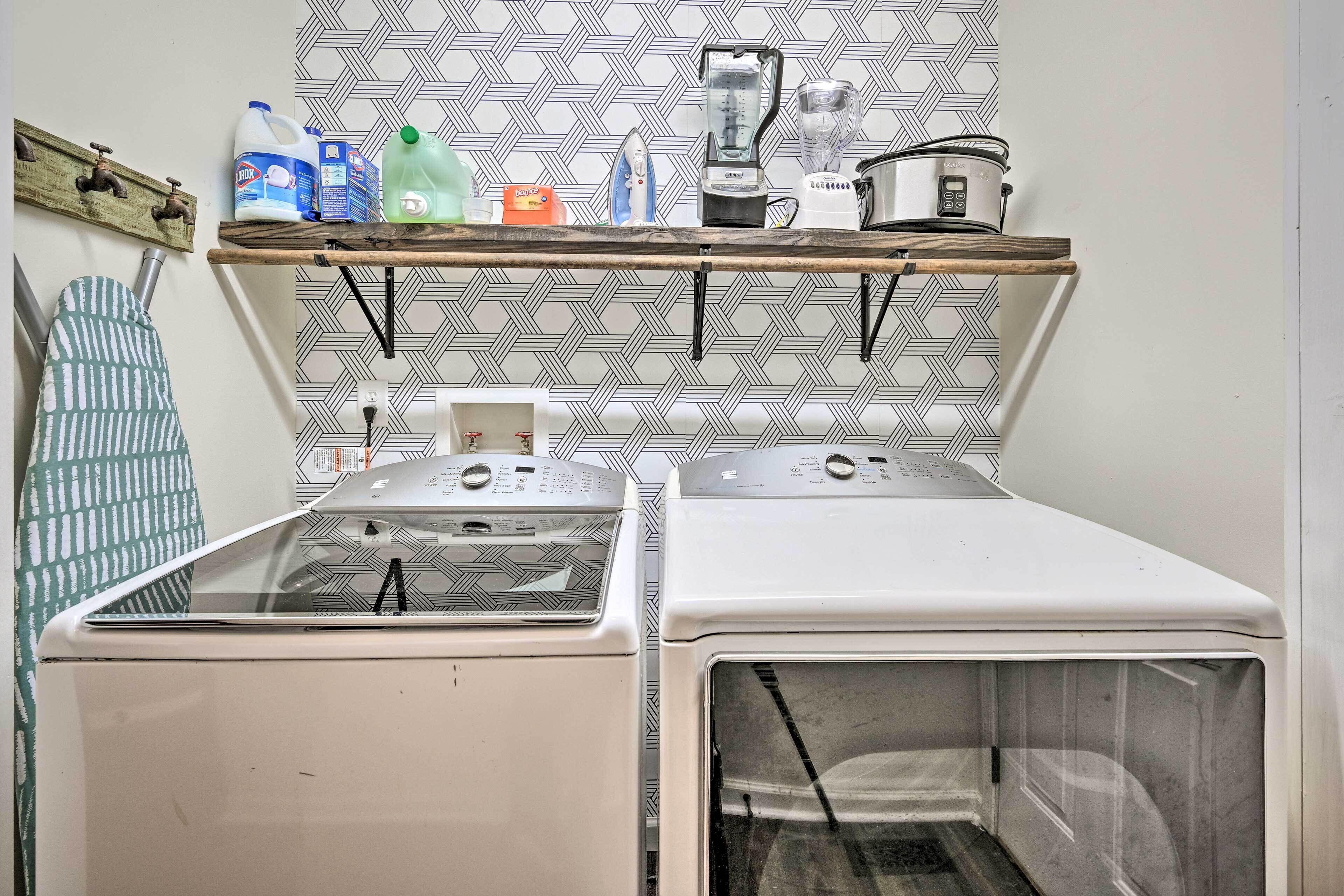 A laundry area with two washing machines, a shelf with cleaning supplies, and a patterned backsplash.