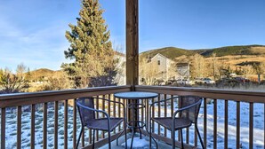 Un balcon avec deux fauteuils en osier et une petite table ronde, d’où l’on peut admirer un paysage enneigé parsemé de maisons et de collines.
