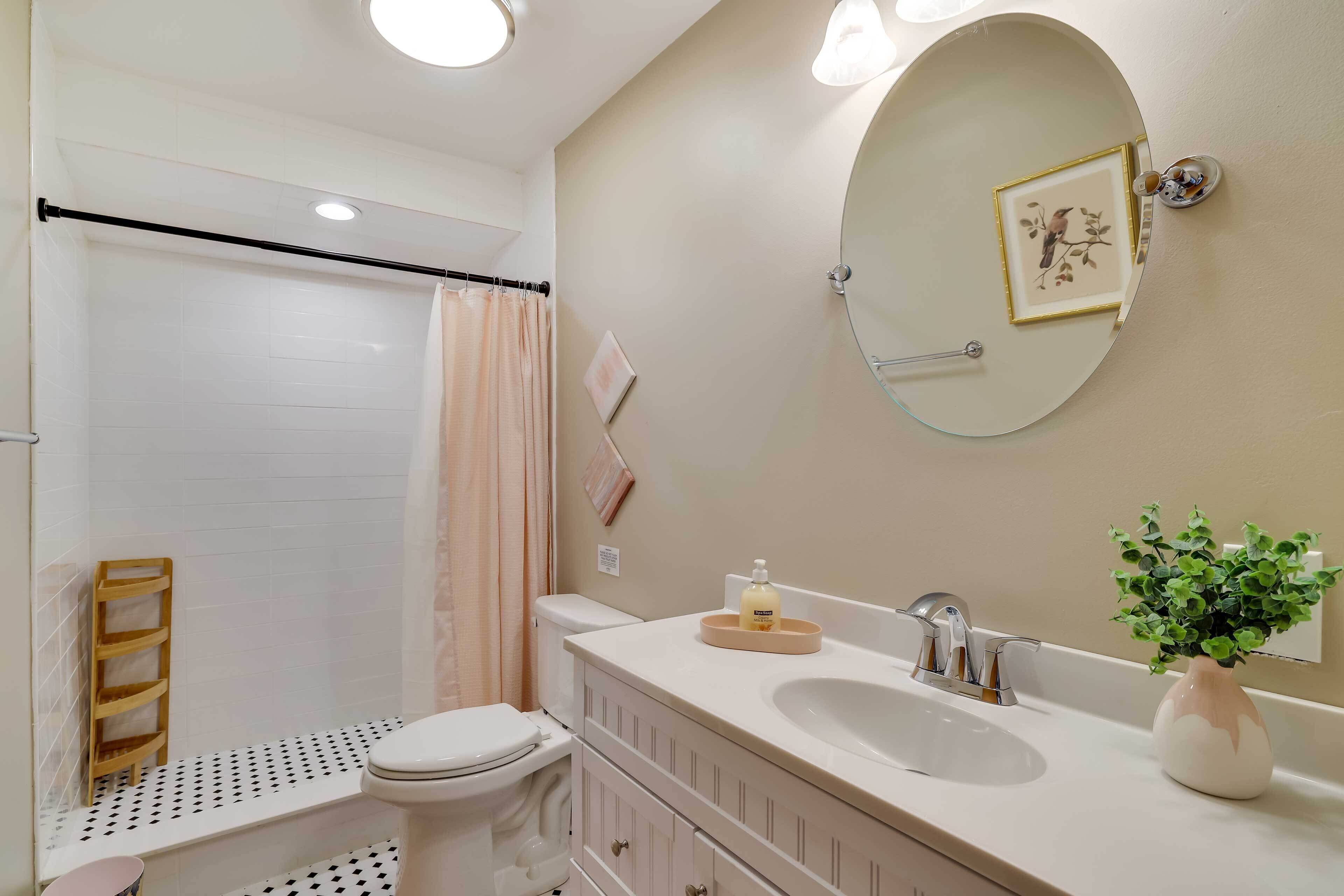 A bathroom with a toilet, sink, mirror, and shower area.