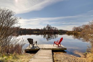 Un molo in legno che si protende in un lago tranquillo, con due sedie: una nera e una rossa.