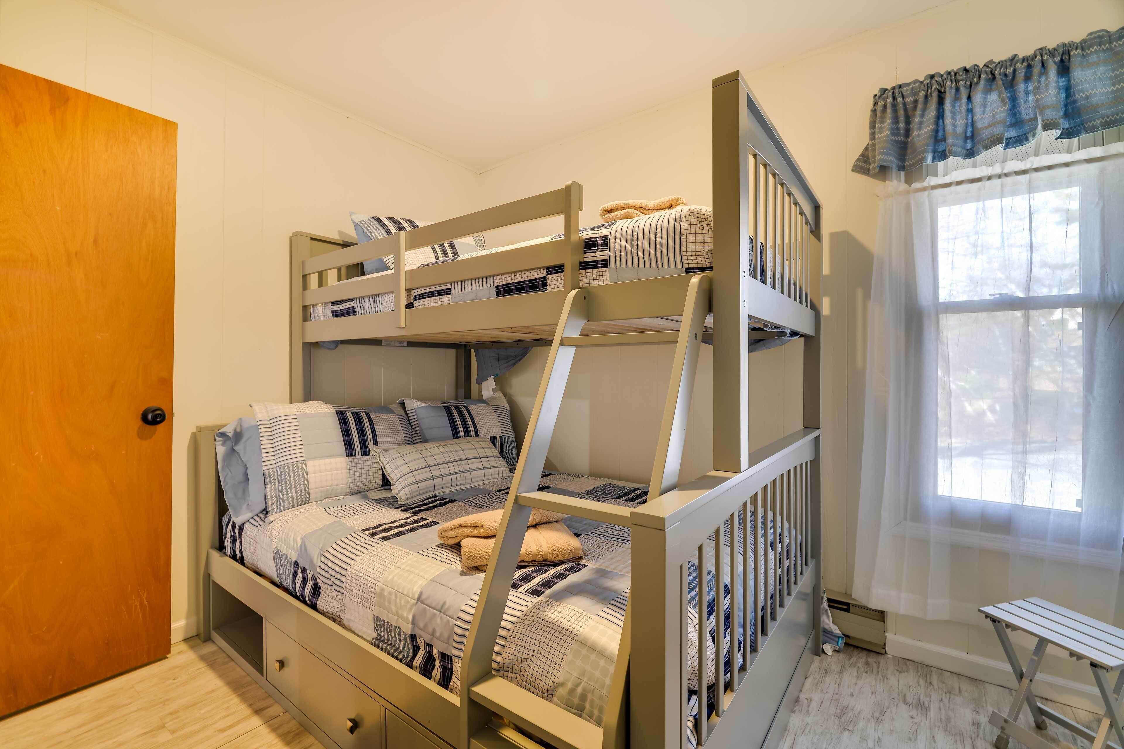 A bunk bed room with a wooden door, a small table, and a window with sheer curtains.