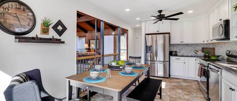 A modern kitchen with white cabinets, stainless steel appliances, and a dining area with a wooden table and chairs.