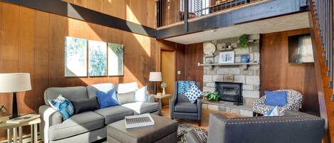 A spacious living area with a fireplace, a sofa set, and a high ceiling with a chandelier.