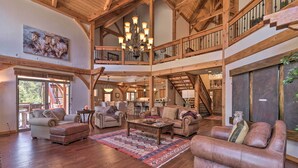 A spacious living area with a high ceiling, wooden beams, a chandelier, and a large window. - Grand Angel Fire Retreat w/ Hot Tub & Fire Pit! (Angel Fire)