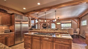 A spacious kitchen with granite countertops, wooden cabinets, a stainless steel refrigerator, and a large island with a gas stove. - Grand Angel Fire Retreat w/ Hot Tub & Fire Pit! (Angel Fire)