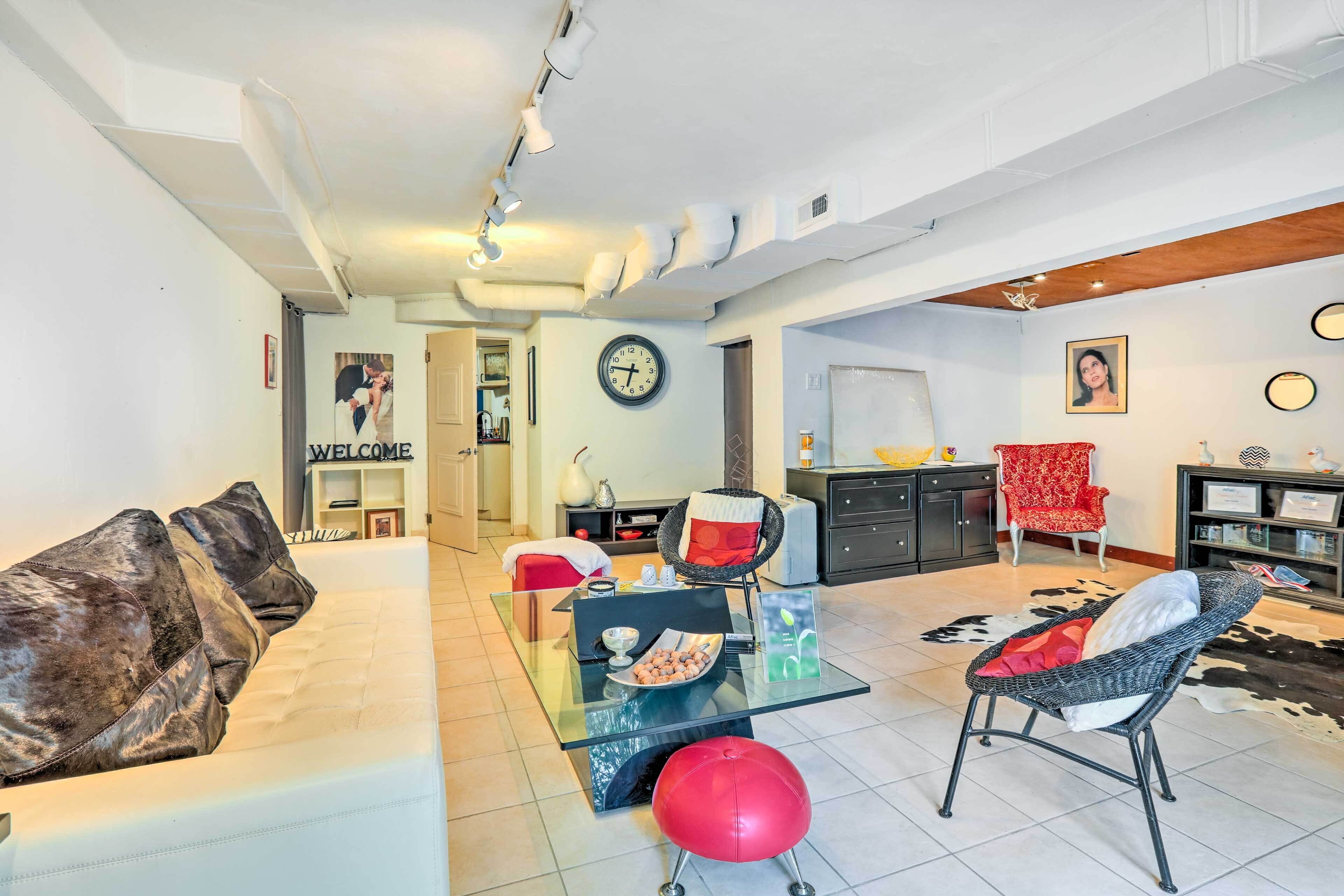 A modern living room with a glass coffee table, a red stool, and a sofa with decorative pillows.
