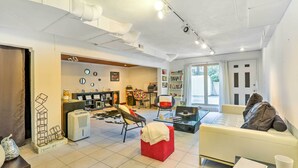 A spacious living room with a sofa, a red ottoman, and a glass coffee table. There is a kitchen area with a refrigerator and a microwave. The room has a modern design with white walls and a tiled floor. - Contemporary Cincinnati Apt w/ Wifi, Near Kenwood! (Cincinnati)