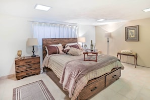 Un dormitorio con cama de madera, mesitas de noche, lámpara, un cuadro enmarcado en la pared y una ventana con cortinas.