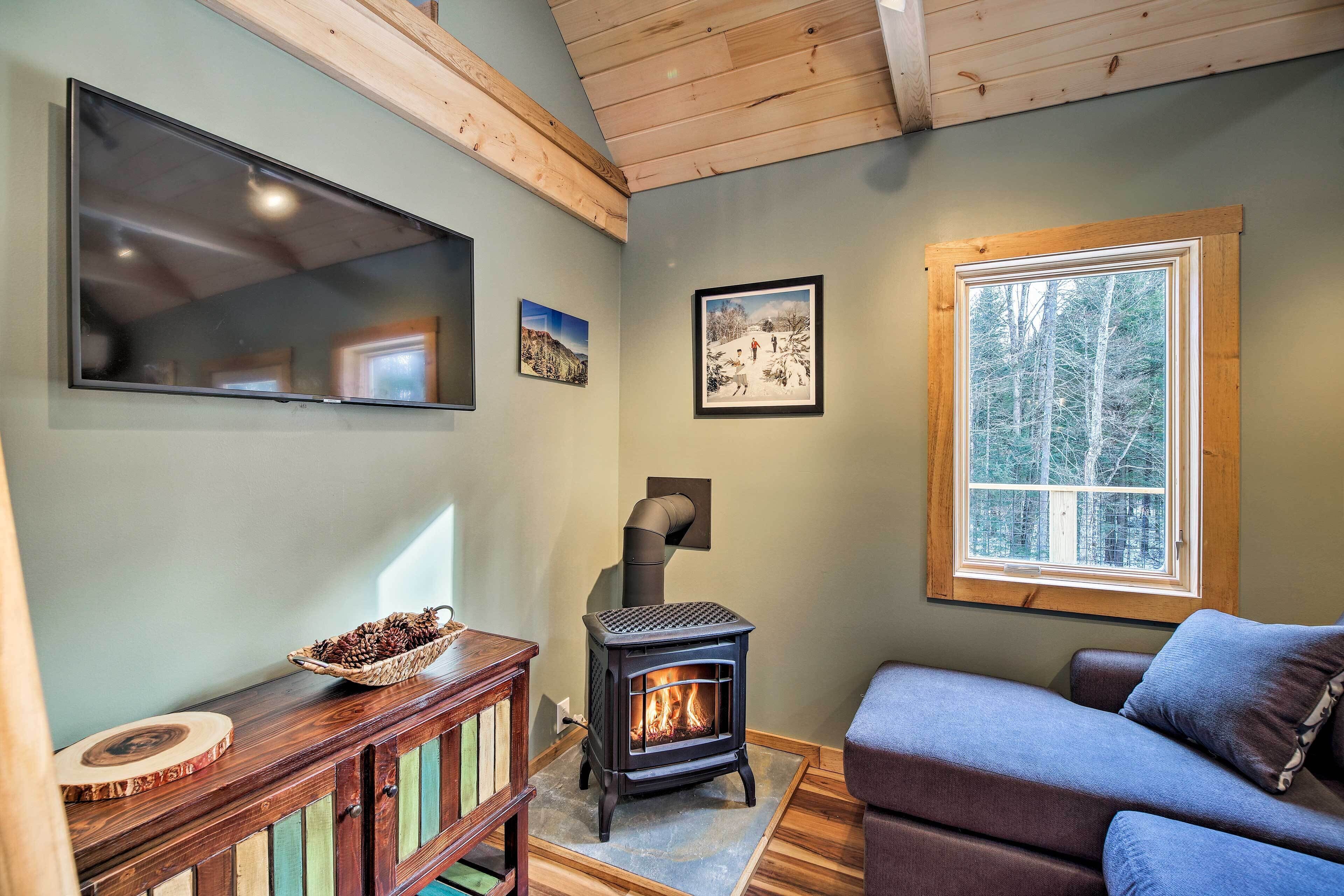 A cozy living room with a fireplace, a large window, and a television mounted on the wall.