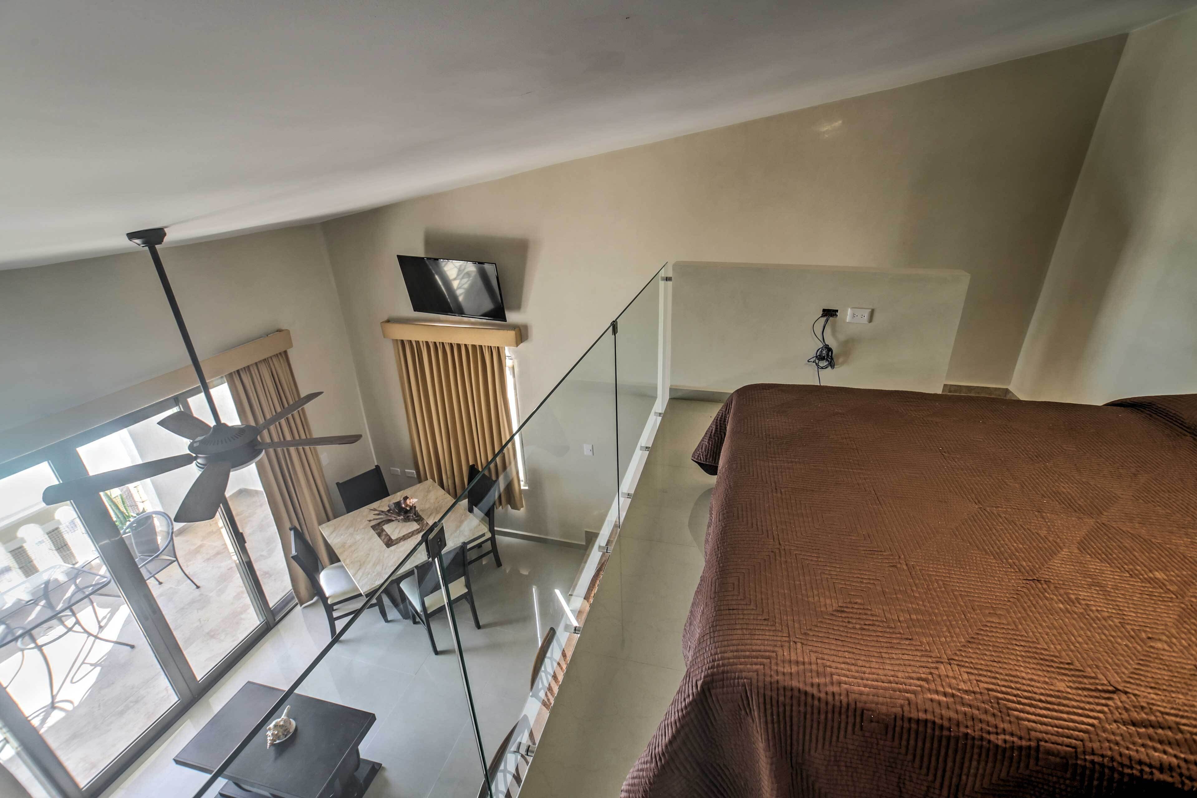 Une pièce comprenant un lit, un bureau, une chaise, un téléviseur posé sur un meuble et une fenêtre avec des rideaux.
