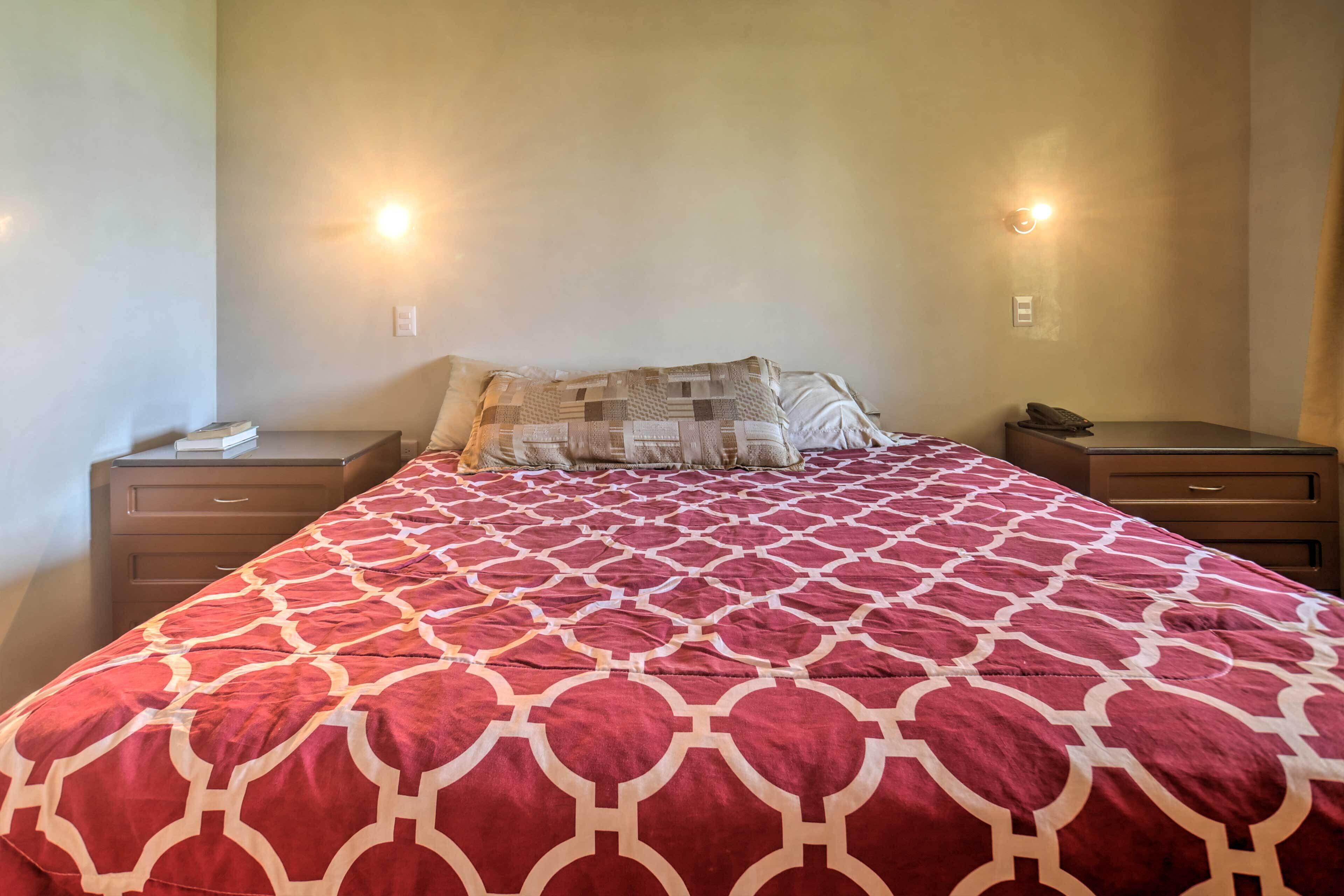 A neatly made bed with a patterned bedspread, two bedside tables with lamps, and a wall-mounted light fixture.