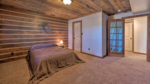Un dormitorio con techo de madera, una cama con manta, una mesita de noche con lámpara y una puerta que da a otra habitación.