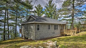 A cabin with a deck, surrounded by trees and a lake.