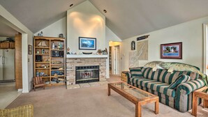 A spacious living room with a fireplace, a striped sofa, a wooden coffee table, and a bookshelf filled with various items.