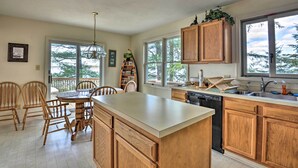 A kitchen with wooden cabinets, a dishwasher, and a large island. There is a dining area with chairs and a table.