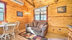 Interior acogedor de una cabaña con techo de madera, un sofá, una mesa de comedor con sillas y un ventanal con persianas.