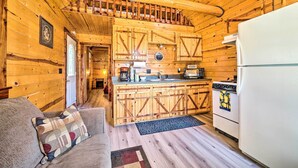 Interior de una cabaña de madera con cocina, una mesa de comedor y un sofá con cojín estampado.