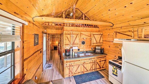 Interior rústico de cabaña con detalles de madera, una cocina con estufa y fregadero, y un ventanal grande en el lado izquierdo.