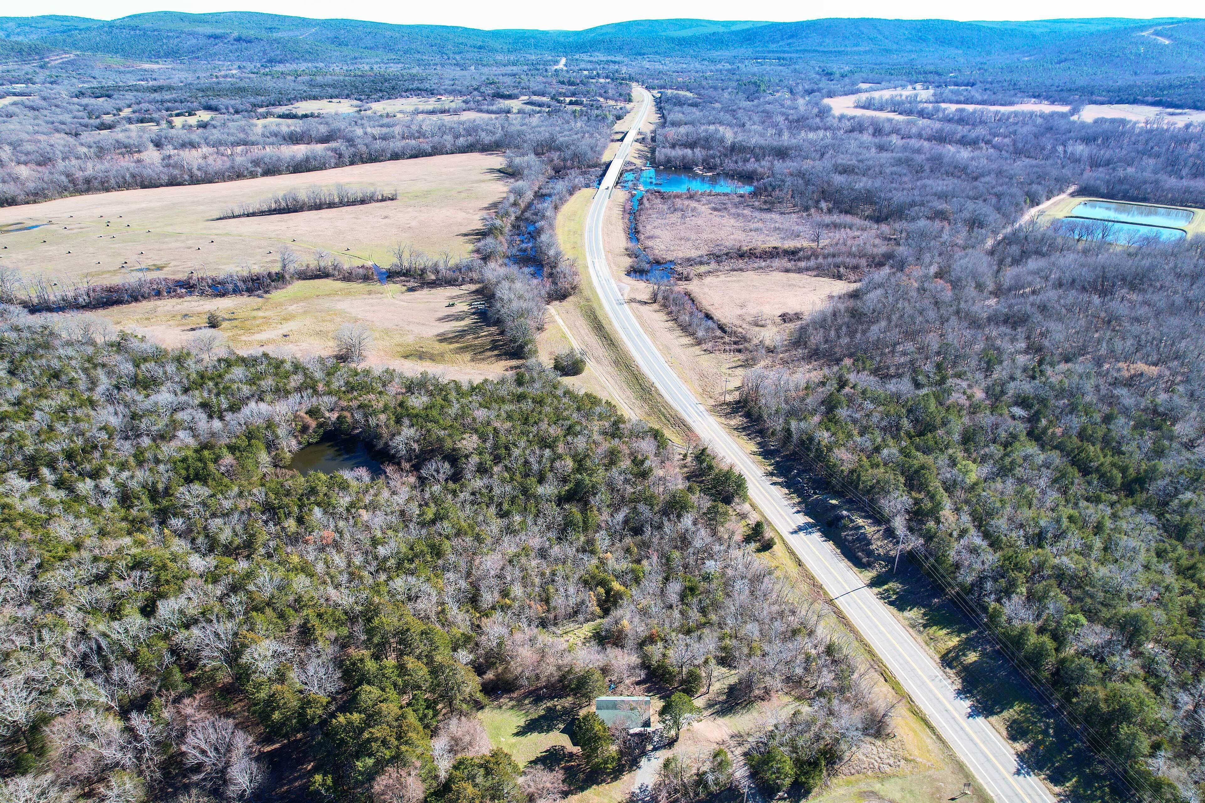 An aerial view of a rural road winding through a forested area with a small building and a blue water body.