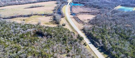 An aerial view of a rural road winding through a forested area with a small building and a blue water body.
