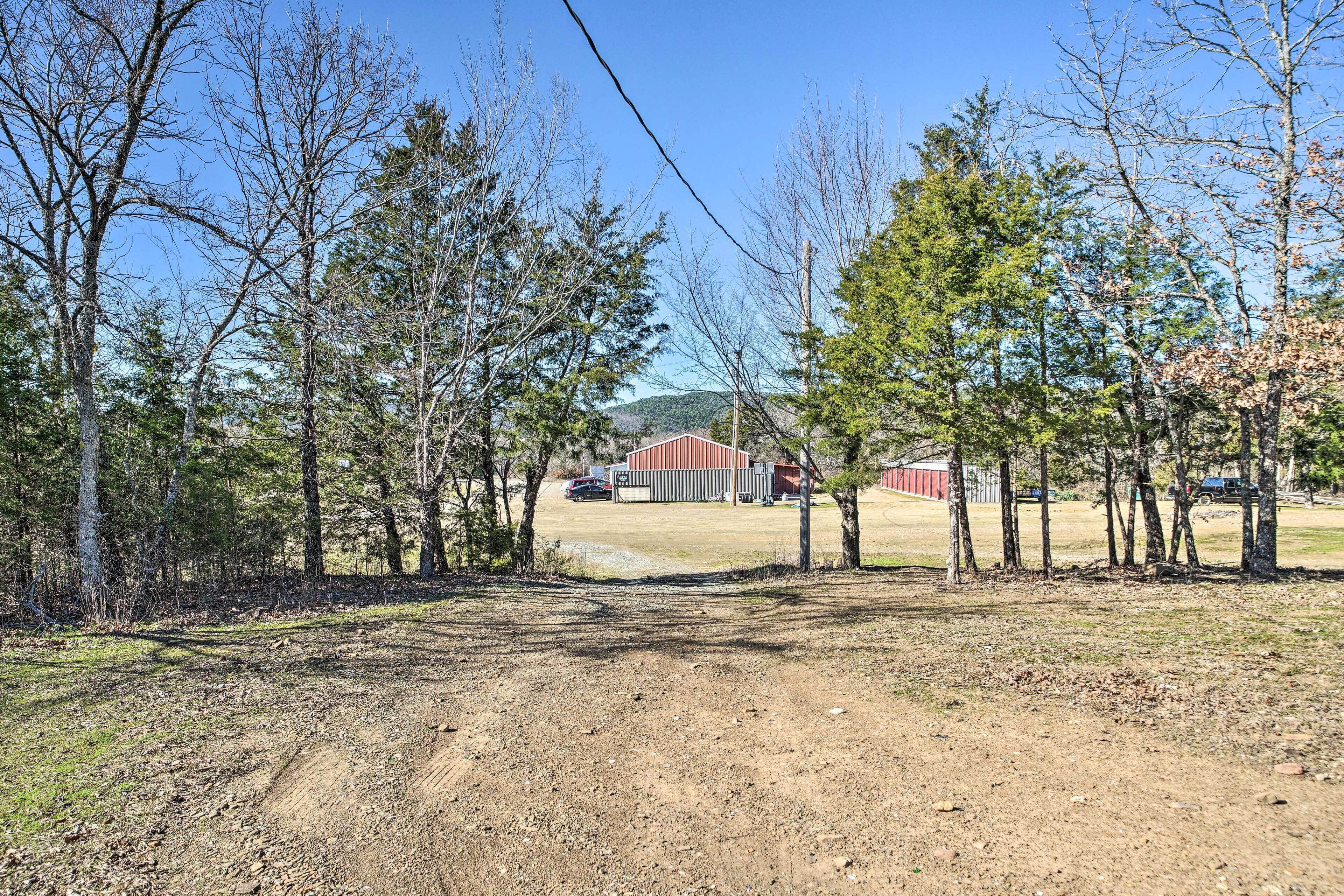 A dirt path leading to a building with a red roof, surrounded by trees and a clear sky.