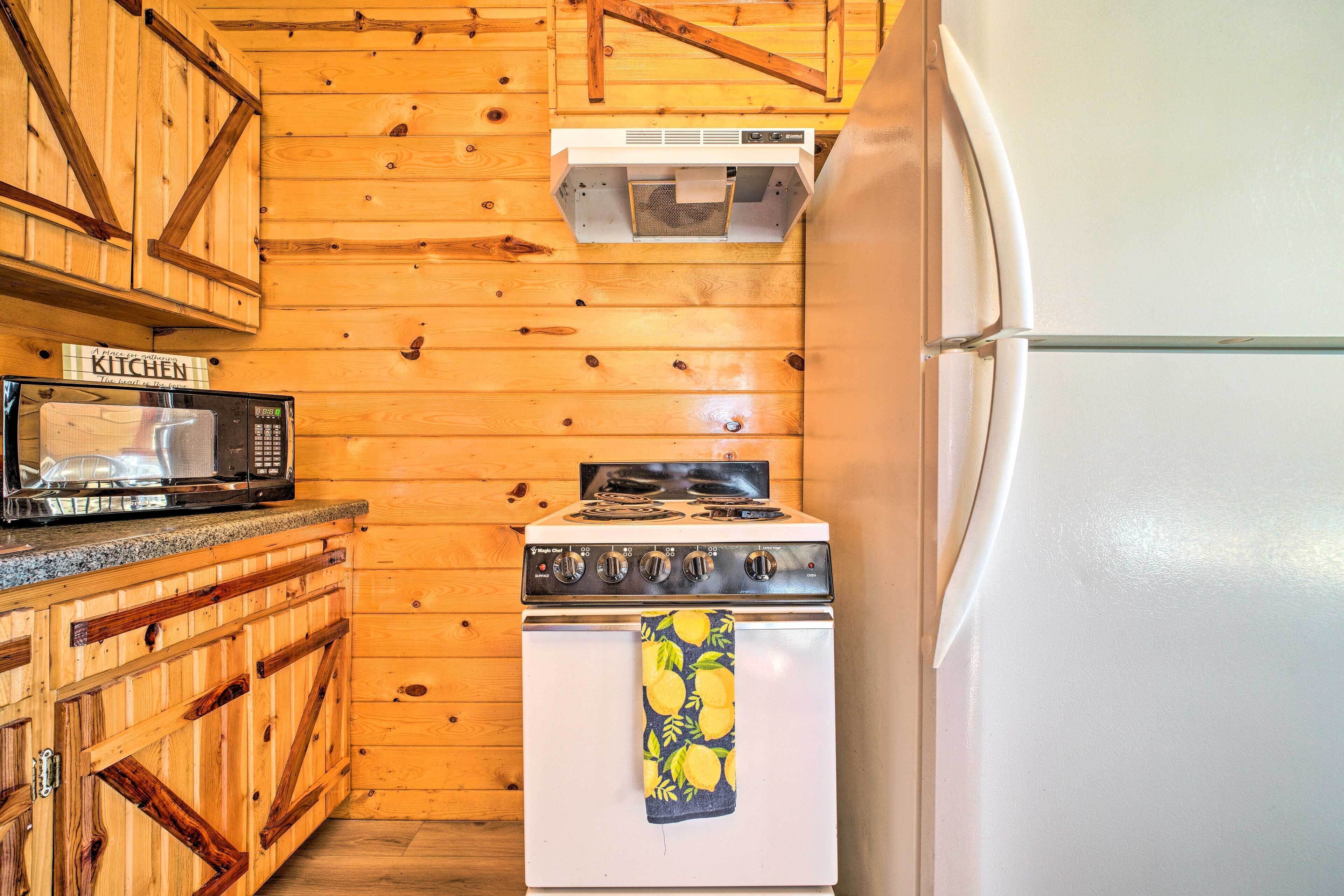 A kitchen with wooden walls, a microwave, stove, and a refrigerator.