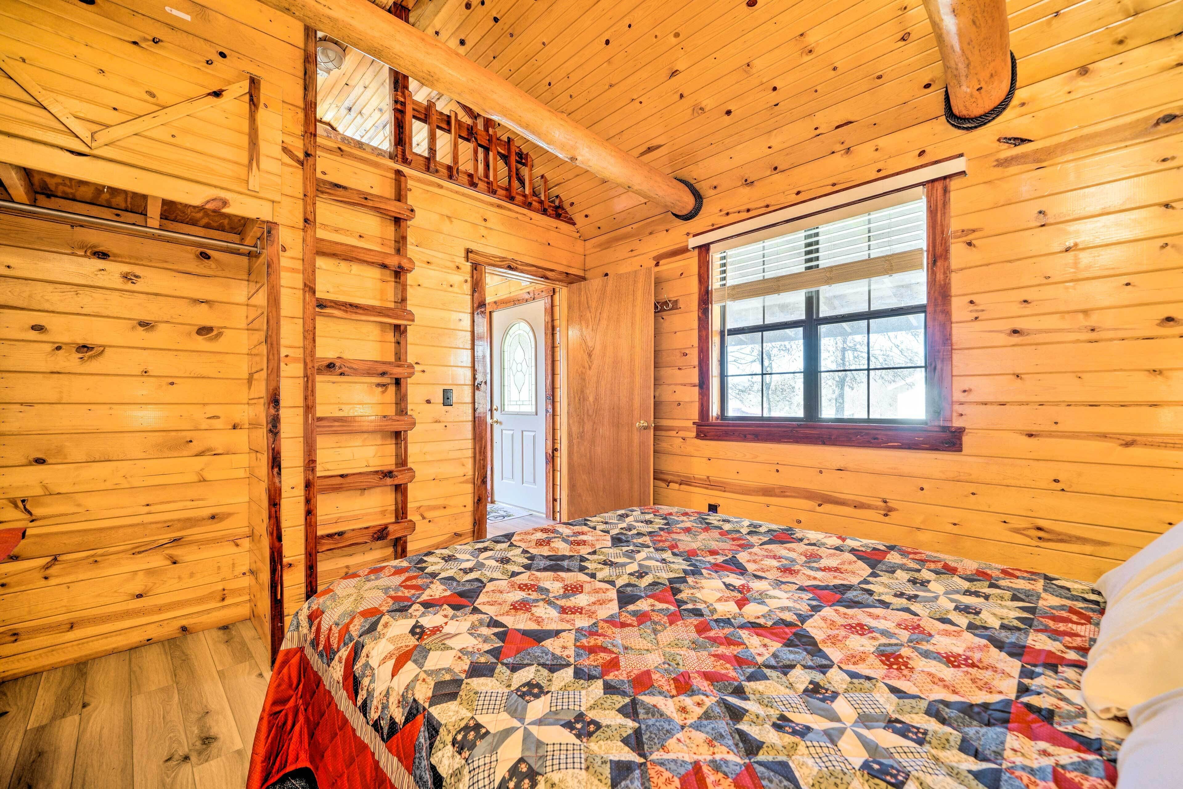 Een slaapkamer in een houten blokhut met een bed, een raam, een deur en een houten trap.