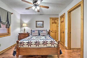 A bedroom with a wooden bed, a ceiling fan, a nightstand with a lamp, and a wooden door. - Pigeon Forge Cabin w/ Hot Tub, 12 Mi to Dollywood! (Sevierville)