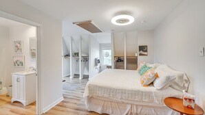 A bedroom with a large bed, a wooden floor, a small table with a tissue box, and a closet with hanging clothes. - Epic Brunswick Apartment With Hot Tub! (Brunswick)