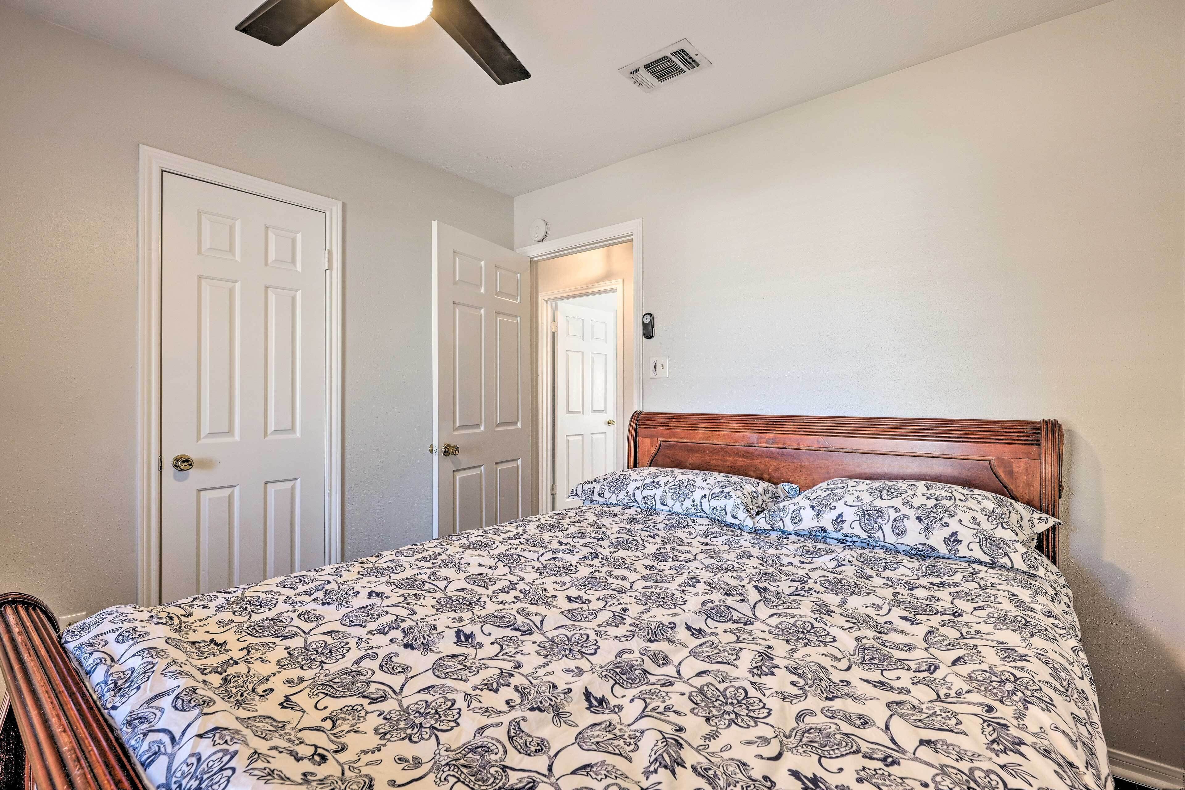 A bedroom with a bed, two doors, a ceiling fan, and a light fixture.