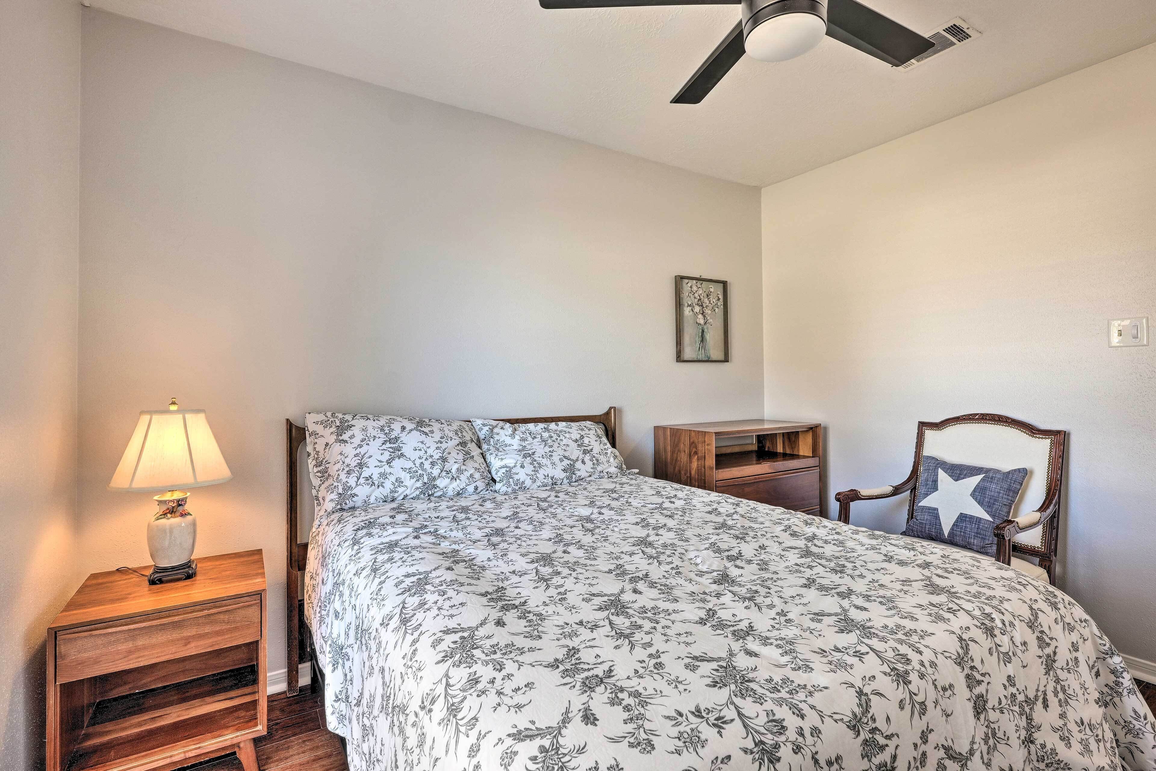 A bedroom with a bed, nightstand, lamp, chair, and ceiling fan.