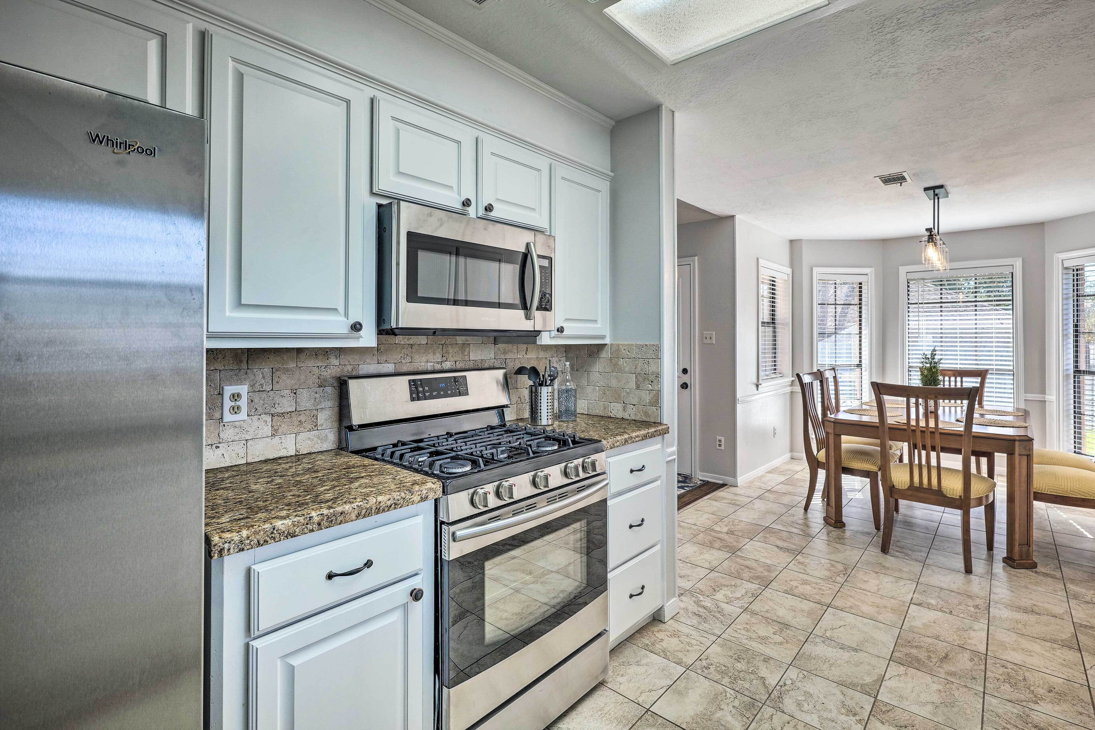 A kitchen with white cabinets, a stainless steel refrigerator, a microwave, a gas stove, and a dining area with a wooden table and chairs.
