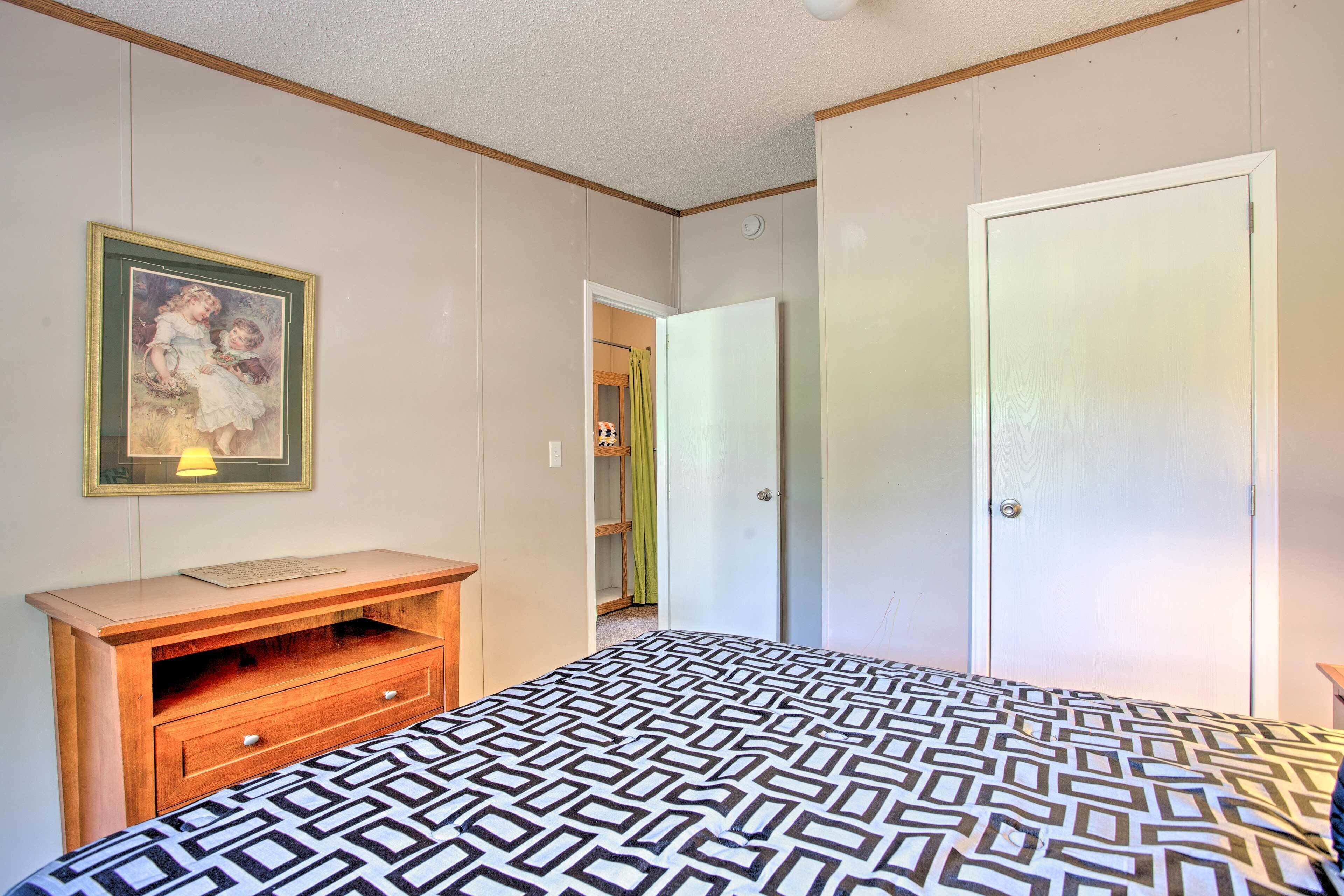 A bedroom with a bed, a wooden dresser, a framed picture on the wall, and a closet with a door.