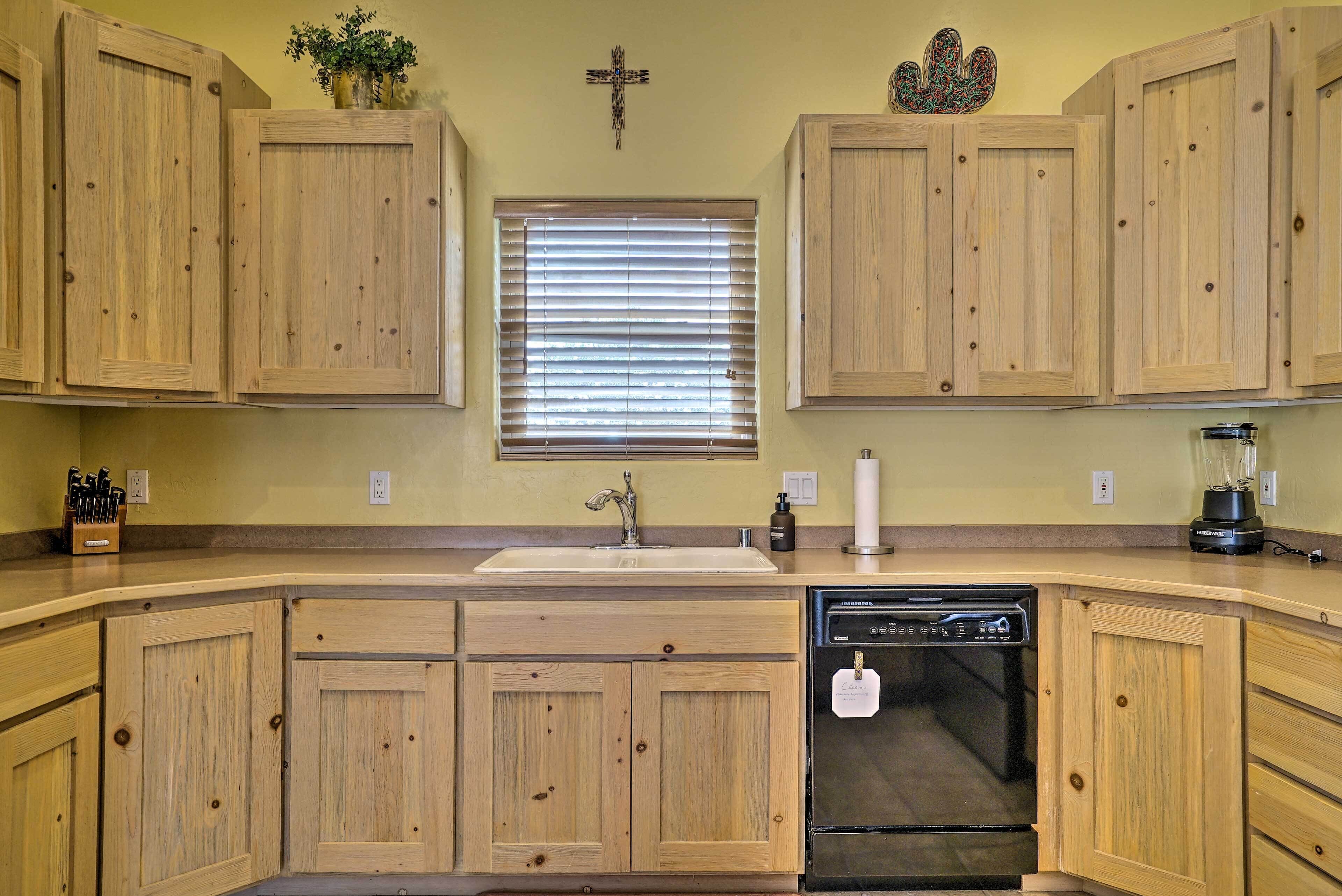 Una cocina con armarios de madera, una ventana con persianas, un lavamanos, un lavavajillas y una licuadora.