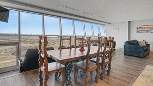 Une salle de conférence avec une grande table et des chaises, de grandes fenêtres donnant sur un aéroport, et un canapé bleu à l’arrière-plan.