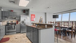 Une cuisine moderne avec des meubles gris, des appareils en acier inoxydable, un grand îlot central et un coin repas avec des chaises en bois.