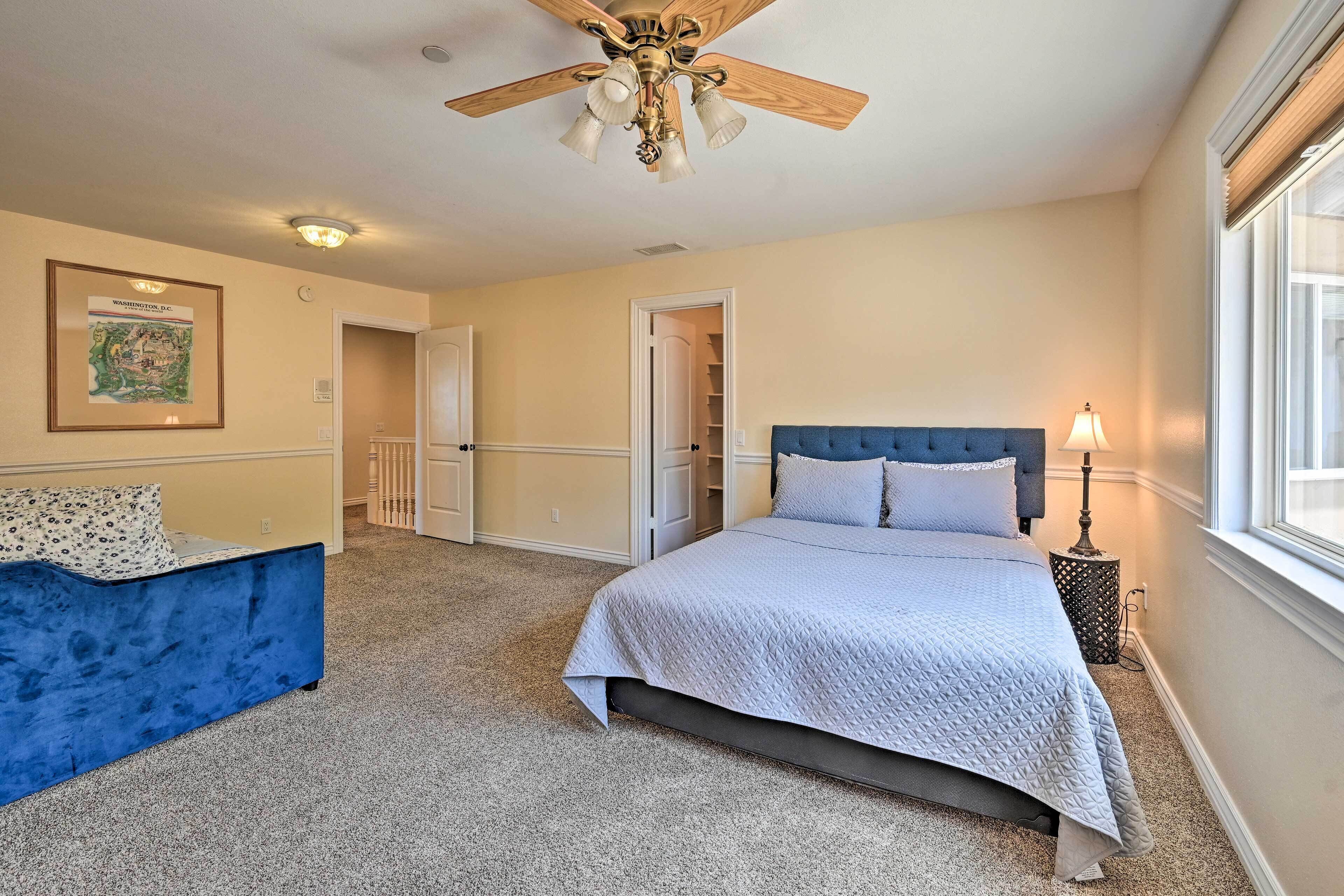 A bedroom with a bed, a blue chair, a ceiling fan, a lamp, and a window.