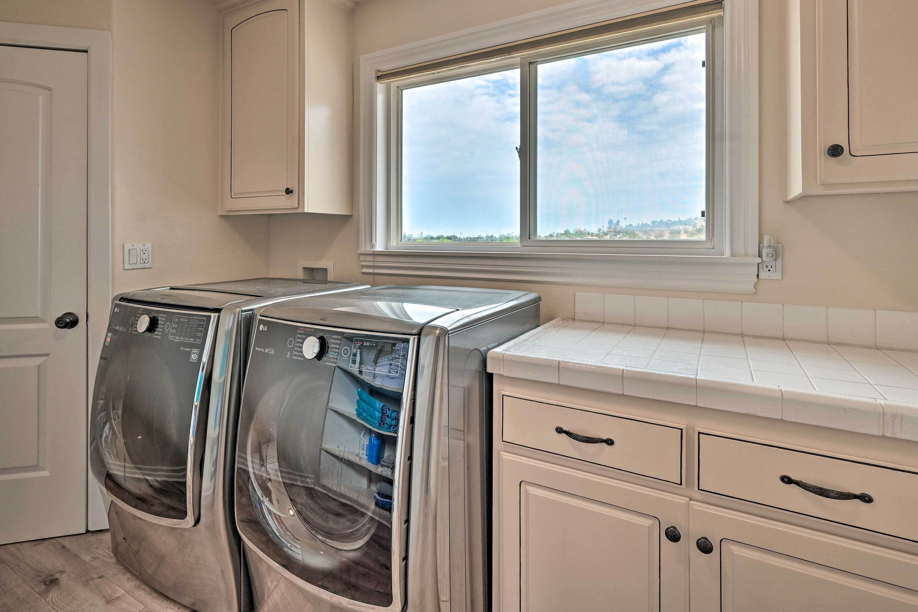 A laundry room with two front-loading washing machines, a window with a view of the outdoors, and a tiled countertop.