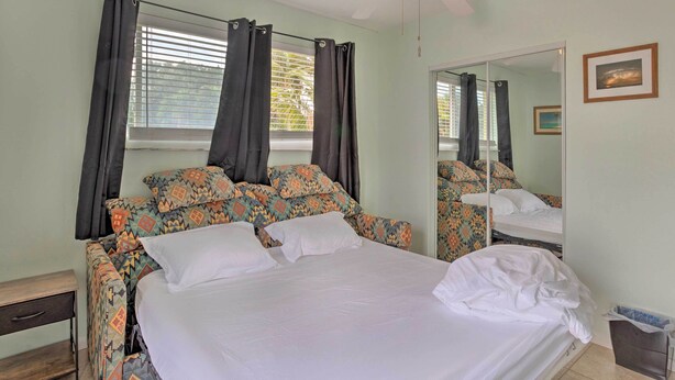 A bedroom with a bed, a nightstand, a mirror, and a window with curtains.