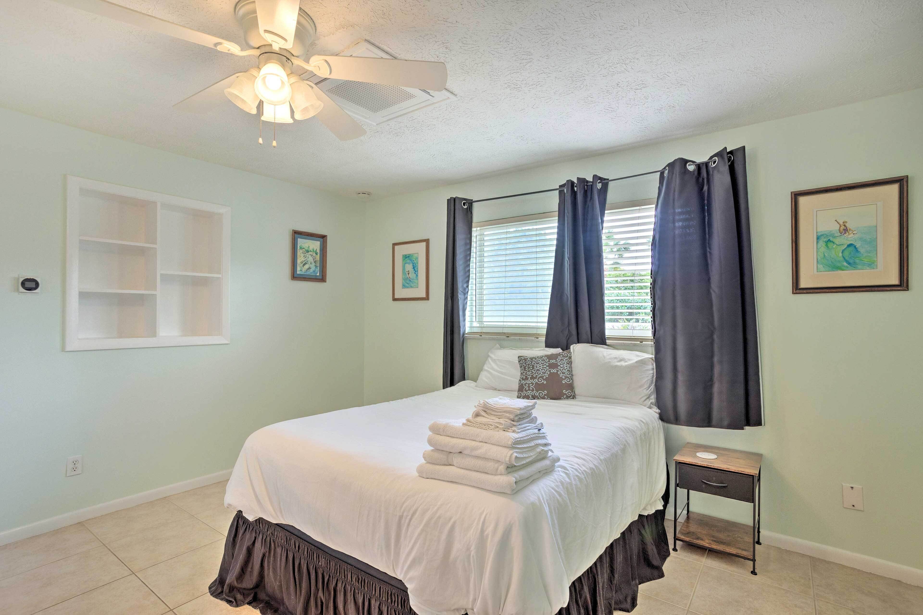 A bedroom with a bed, a nightstand, a ceiling fan, and a window with curtains.